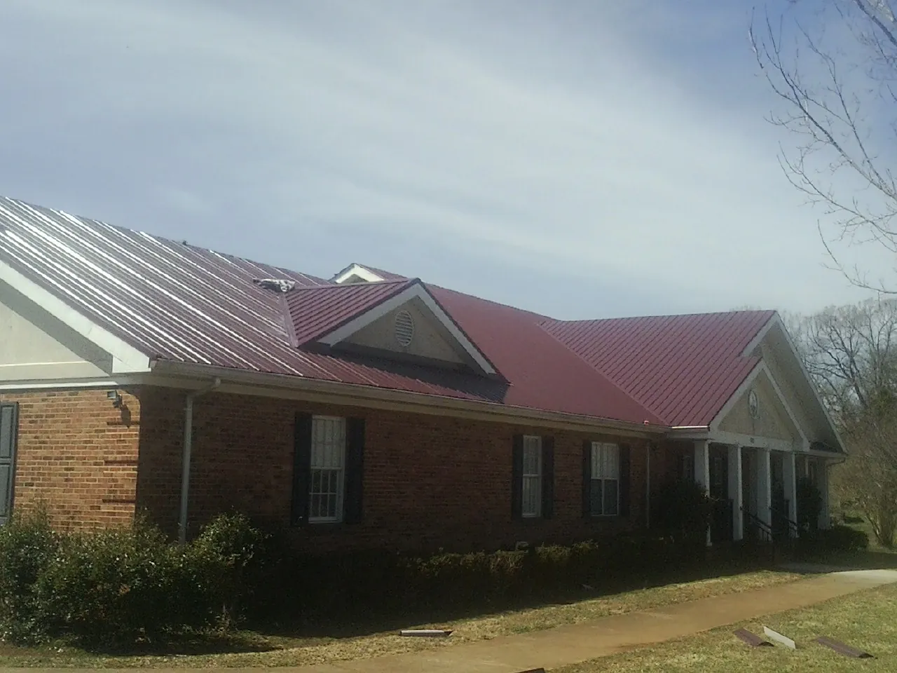 Red metal roof with gabled entries on a long brick building, from a Hail Damage Roof Repair job in Rich Hill