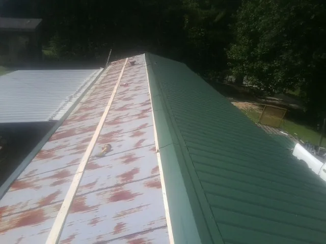 Old rusted panels beside newly installed green metal roofing — Wind Damage Roof Repair by Roofing Brothers in Rich Hill