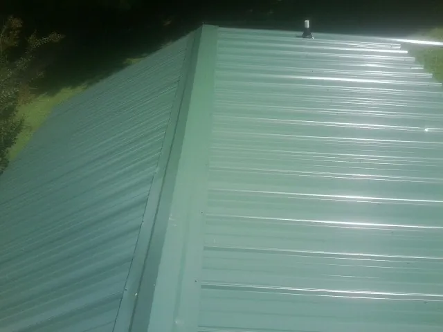 New green metal panels meeting at the ridge of a roof — Flat Roof Repair work by our crew in Rich Hill