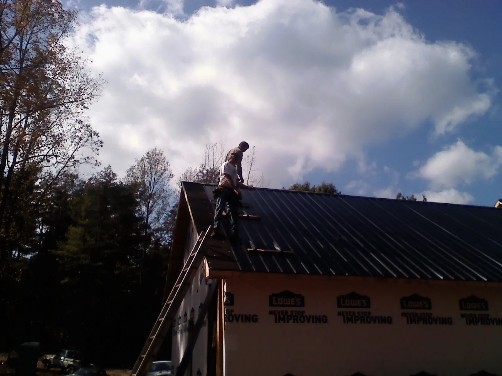 Roofer fastening dark metal panels high against a cloudy sky, from a Roof Inspection job in Rich Hill