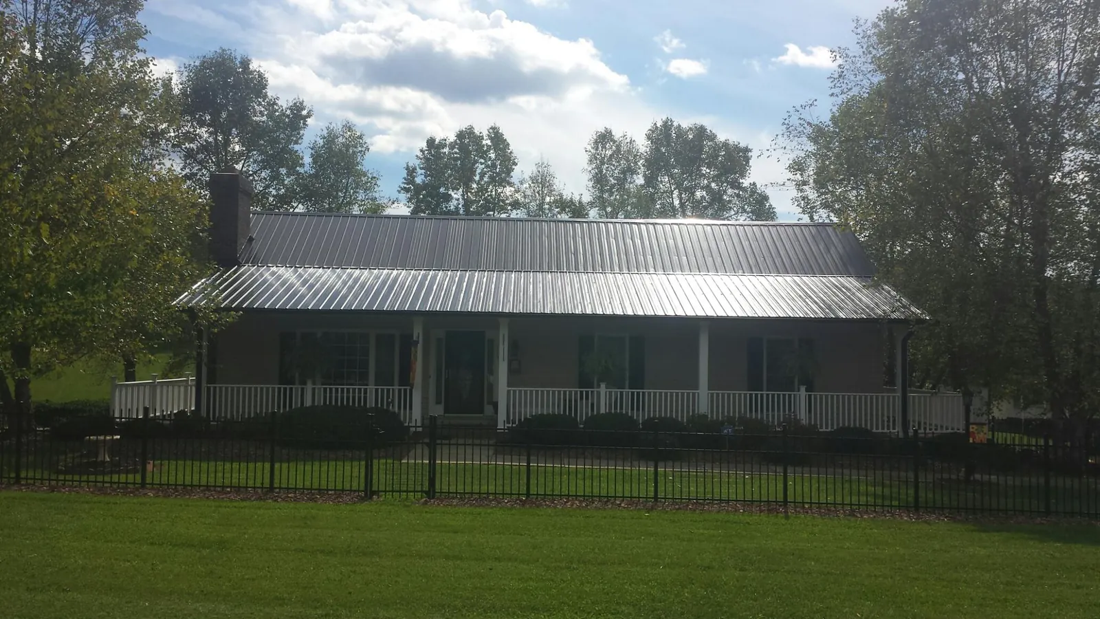 Gray metal roof on a brick ranch with a full width front porch — Gutter Guard Installation work by our crew in Rich Hill