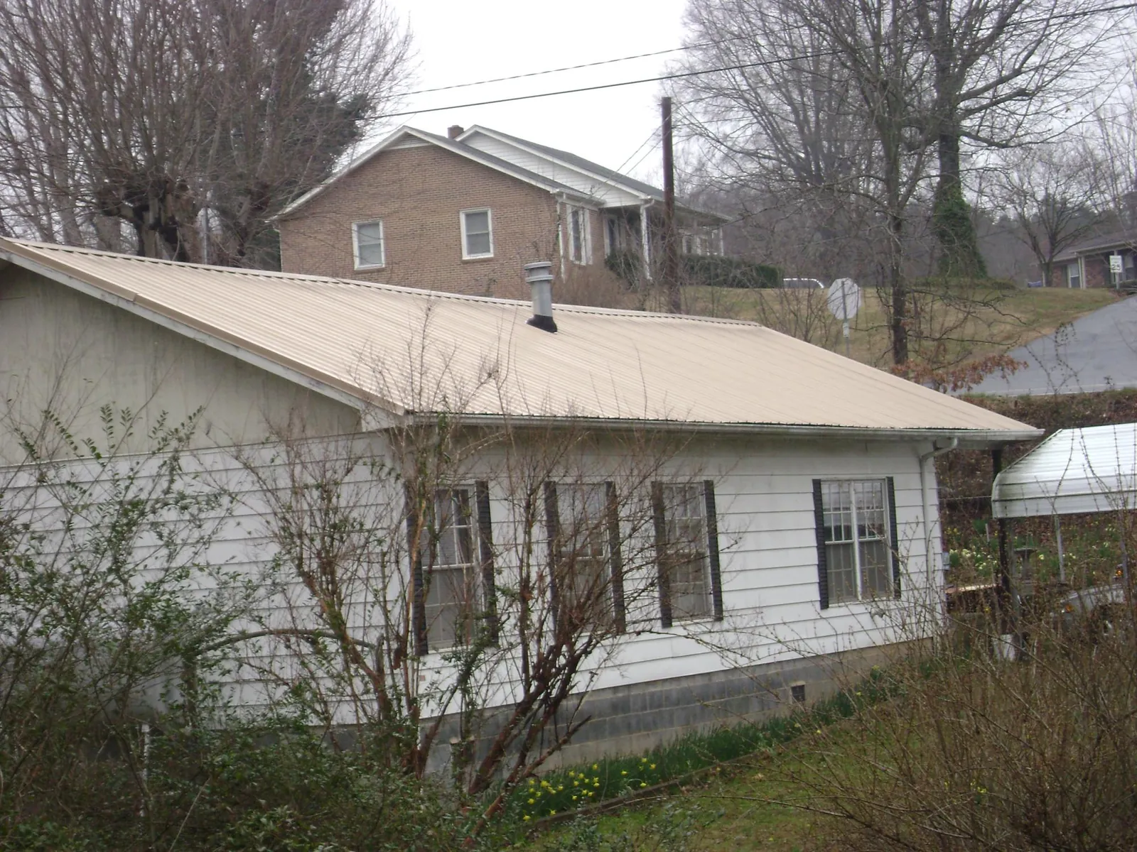 Tan metal roof on a white sided house set into a hillside — Commercial Roofing by Roofing Brothers in Rich Hill