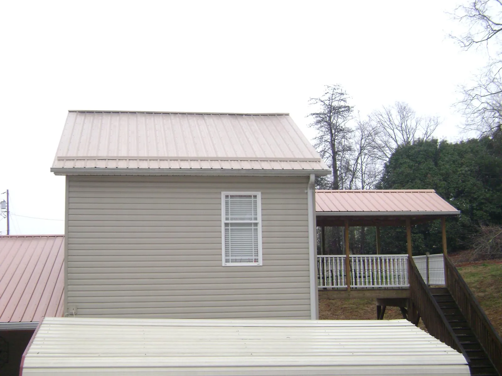 Tan metal roofs on a two story addition and attached porch, from a Roof Replacement job in Rich Hill